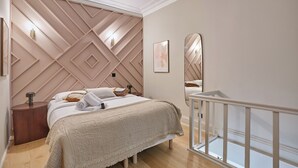 A bedroom with a bed, bedside tables, a nightstand, a mirror, and a white railing. - Charmant Studio Duplex Beaubourg Le Marais (Paris)