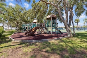 A playground with slides and climbing structures, surrounded by trees and grass.