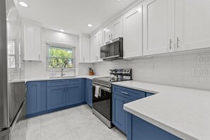 Une cuisine moderne avec des meubles blancs et bleus, des appareils électroménagers en acier inoxydable et une fenêtre donnant sur un paysage verdoyant.