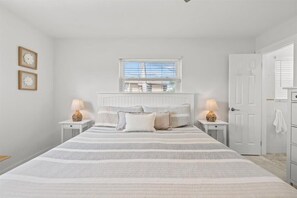 A bedroom with a bed, two bedside tables with lamps, a window, and a door. - Private Heated Pool | Walk to IRB Beach (Indian Rocks Beach)