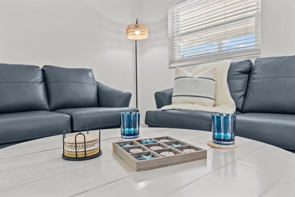 Un salon moderne avec deux canapés gris, une table basse ronde et des objets décoratifs, notamment un chandelier et un plateau avec des bougies.