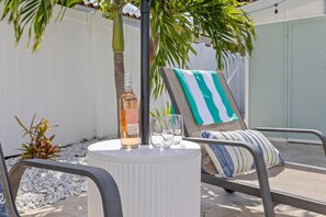 A lounge chair with a striped cushion, a bottle of French wine, and two glasses on a round table.