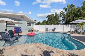 A swimming pool with lounge chairs and umbrellas, surrounded by a white fence and palm trees. - Private Heated Pool | Walk to IRB Beach (Indian Rocks Beach)