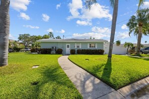 A single-story house with a front yard, a pathway leading to the entrance, and a clear sky. - Private Heated Pool | Walk to IRB Beach (Indian Rocks Beach)