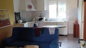 Sala de estar com sofá azul e mesa de centro, cozinha com armários brancos e micro-ondas, e uma porta com chaveiro.