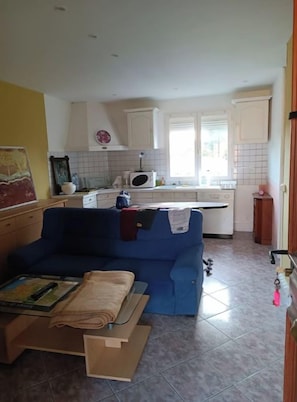 A living room with a blue sofa and a coffee table, a kitchen with white cabinets and a microwave, and a door with a keychain.
