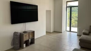 Un saló modern amb un televisor de pantalla plana fixat a la paret, un moble d'emmagatzematge gris i una porta corredissa de vidre que dona a un balcó.