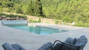 Zona de piscina amb dues cadires mullides i una paret de pedra al fons.