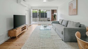 Una sala de estar moderna con un televisor de pantalla plana, un sofá gris, una mesa de centro y un ventilador de techo.