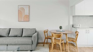Una sala de estar moderna con un sofá gris, sillas de madera, una mesa redonda y una pequeña planta en maceta.