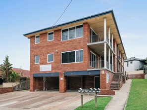 A multi-story brick building with a sign for "Rickley Pear Stays" and a parking area with numbered spaces. - Prickly Pear Stays in Merewether - Ranclaud St, 1-bedroom (Merewether)