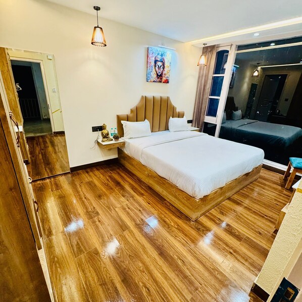 A modern hotel room with a large bed, wooden flooring, a nightstand with a Buddha statue, and a painting above the bed.