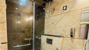 Un baño moderno con ducha envuelta en vidrio, inodoro blanco y lavamanos negro.