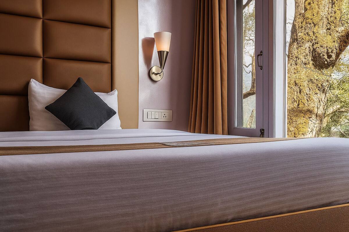 Habitación de hotel con una cama grande, una lámpara de pared, una ventana con cortinas y vistas a árboles.