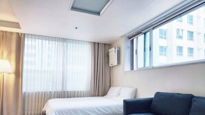 A hotel room with a bed, a sofa, a lamp, and a window with curtains.