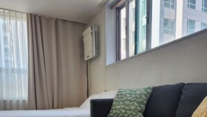A hotel room with a bed, a sofa, a white coffee table, and a window with curtains.