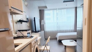 A compact hotel room with a kitchenette, a bed, a small table, and a chair.