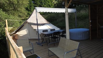 En træterrasse med et telt, et bord, stole og et spabad.
