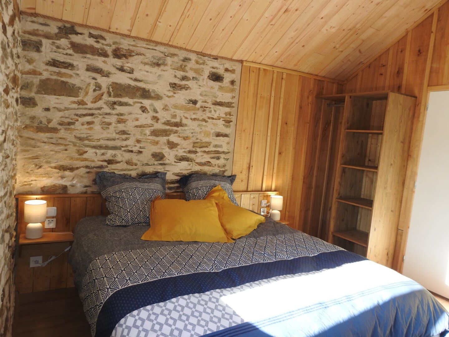Quarto aconchegante com parede de pedra, teto de madeira e cama com roupa de cama estampada.