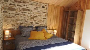 Quarto aconchegante com parede de pedra, teto de madeira e cama com roupa de cama estampada.
