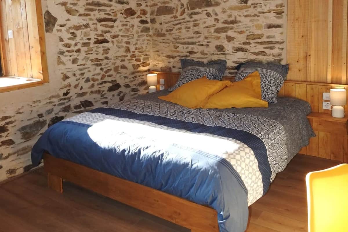 A bedroom with a stone wall, wooden ceiling, and a bed with blue and yellow bedding.