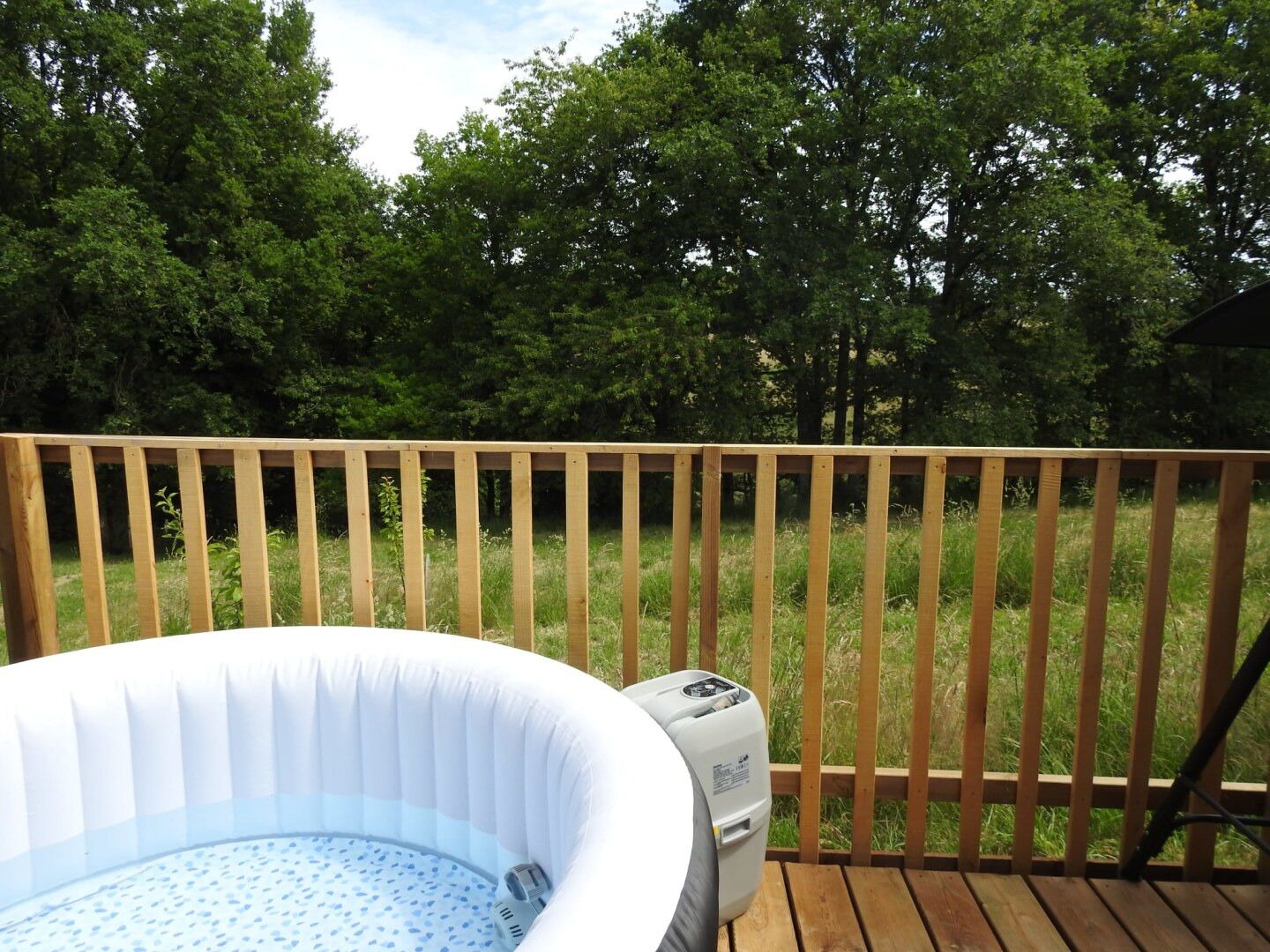 A hot tub on a wooden deck with a grassy background and trees.