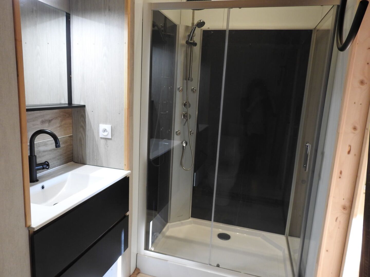 Ein modernes Badezimmer mit einer gläsernen Duschkabine, einem weißen Waschbecken und einem dunklen Waschtisch.