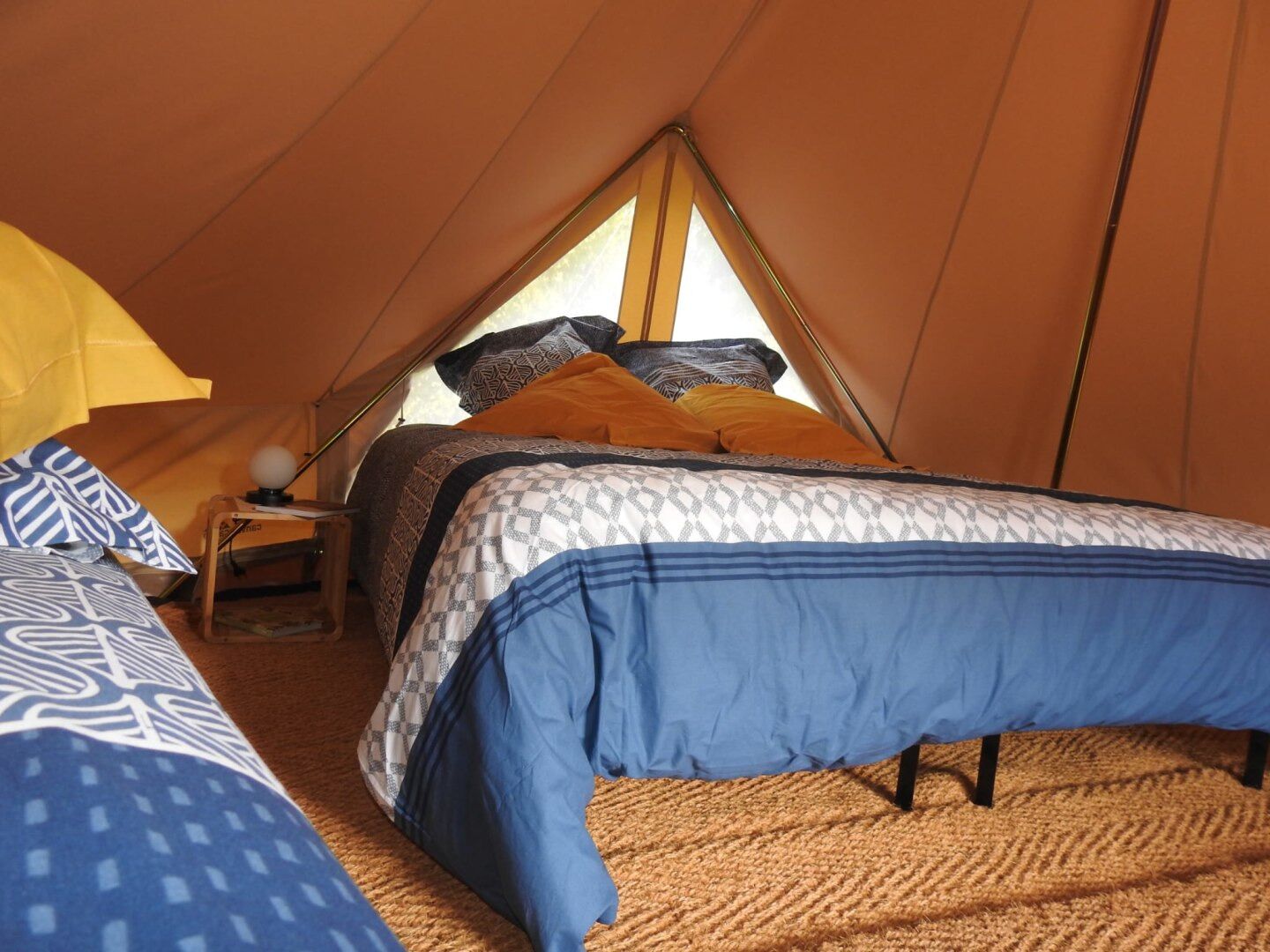 Un cuarto tipo tienda de campaña, acogedor y triangular, con una cama, una mesita de noche y una lámpara.