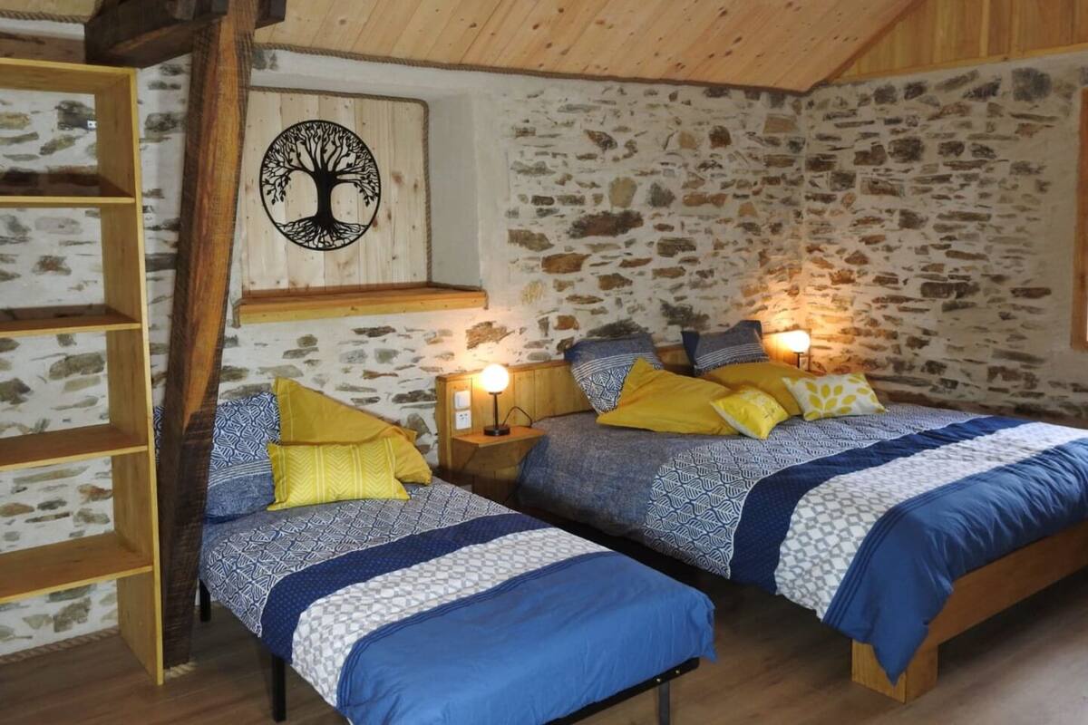 A cozy bedroom with two beds, wooden beams, stone walls, and a tree mural.
