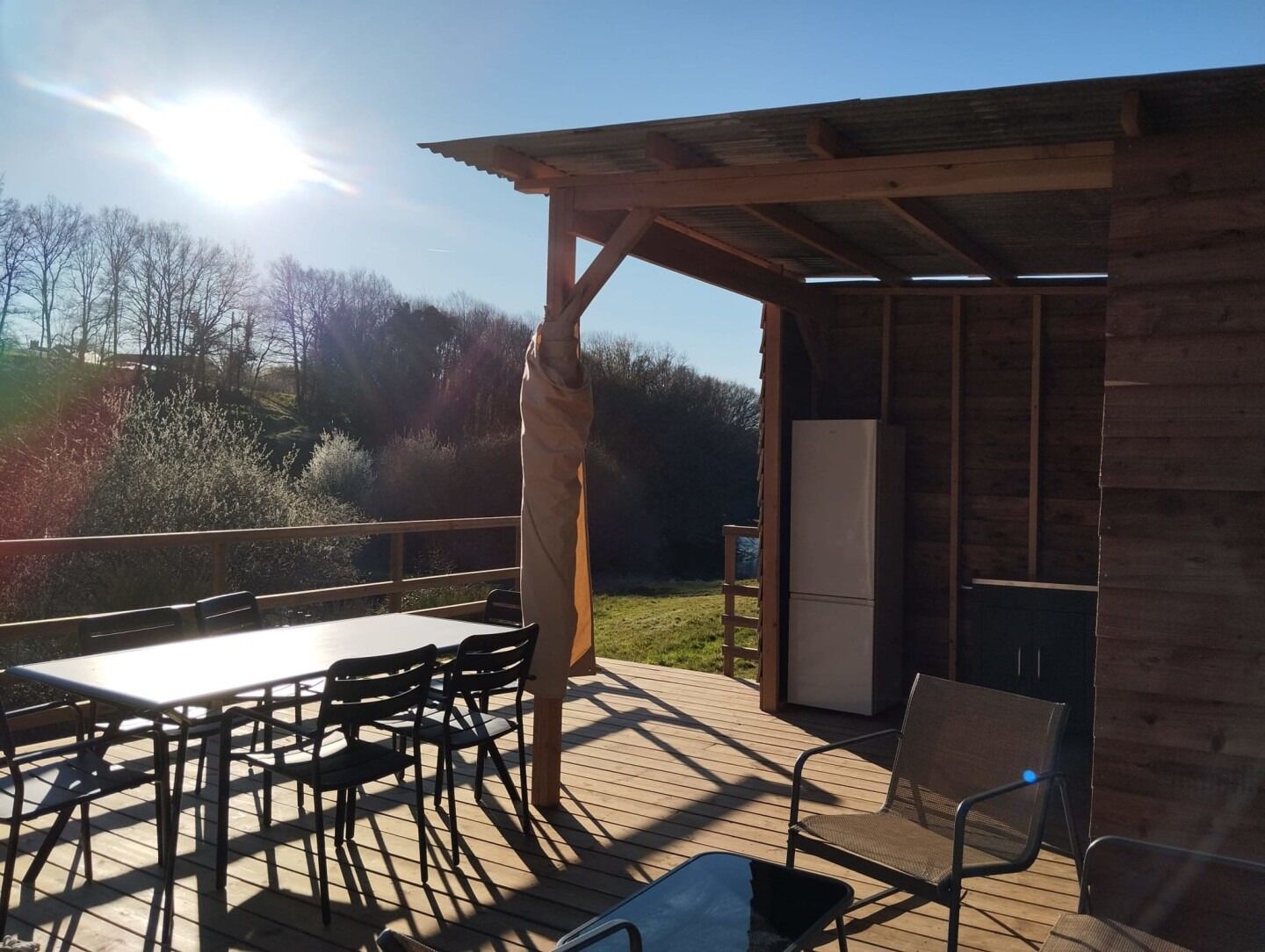 A wooden deck with a table and chairs, a refrigerator, and a pergola structure.