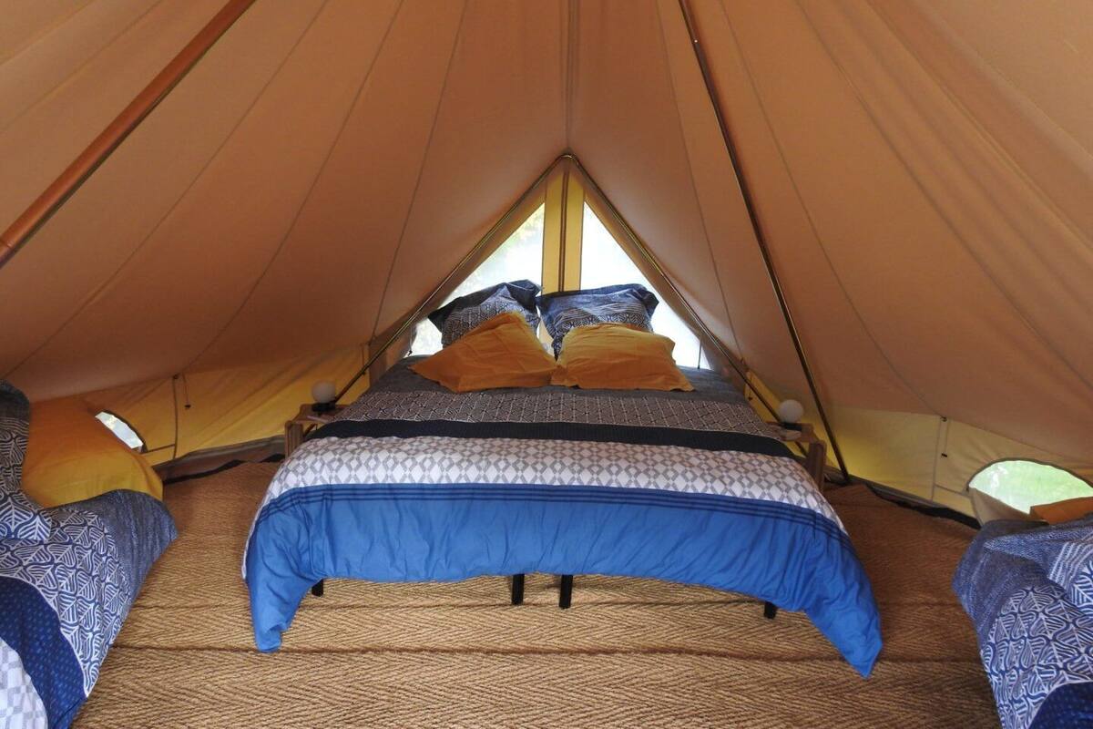 A tent with a pitched roof, a bed with patterned bedding, and a rope-woven floor.
