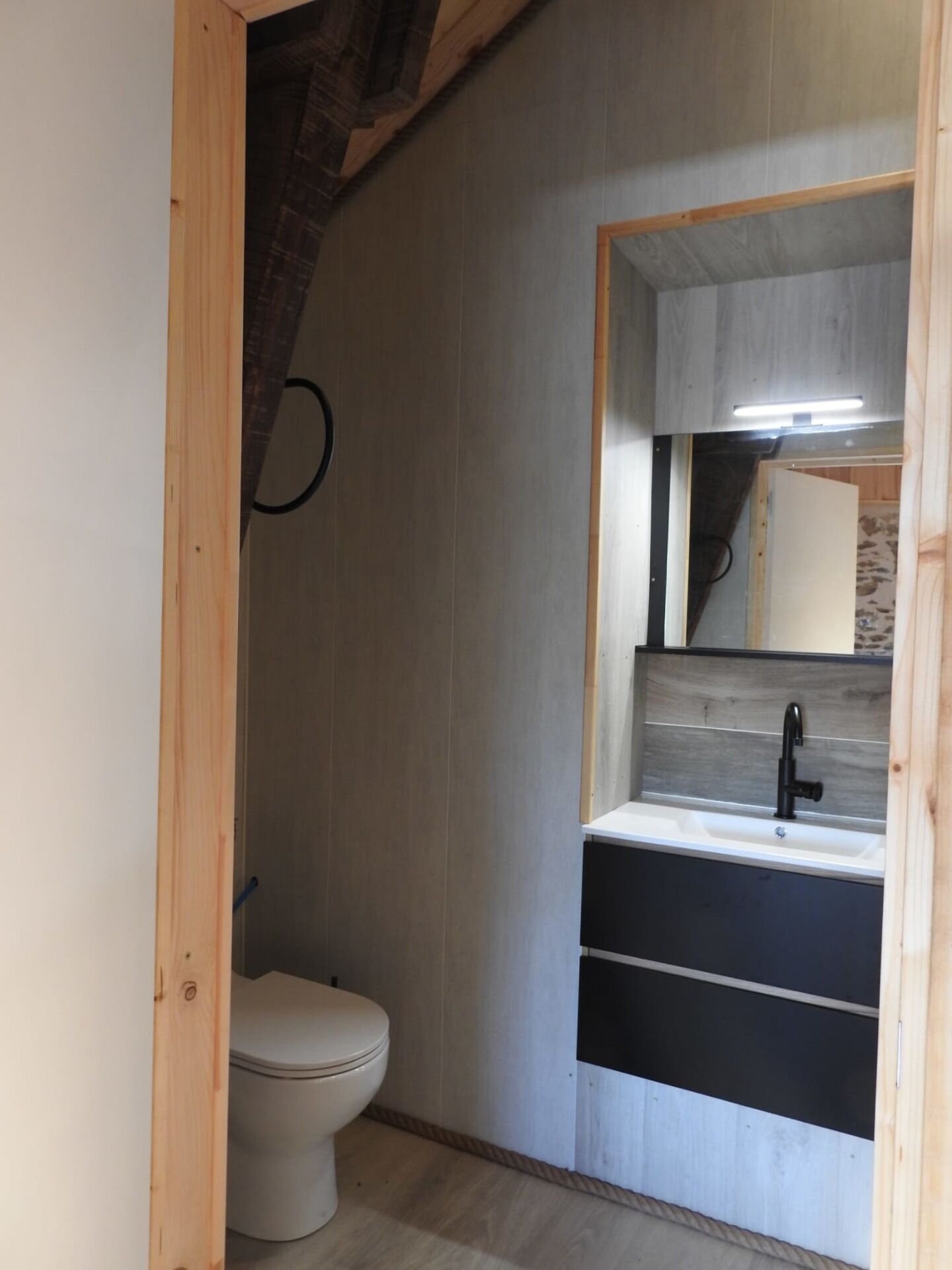 Un bagno piccolo ma funzionale, con il water, un lavabo con specchio e pareti in legno.