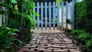 A stone pathway leading to a white gate surrounded by lush greenery. - The Tamarillo (Ooty)