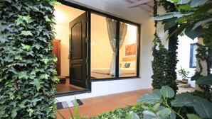A room with a sliding glass door, a bed with a colorful blanket, and a small potted plant on the windowsill. - The Tamarillo (Ooty)