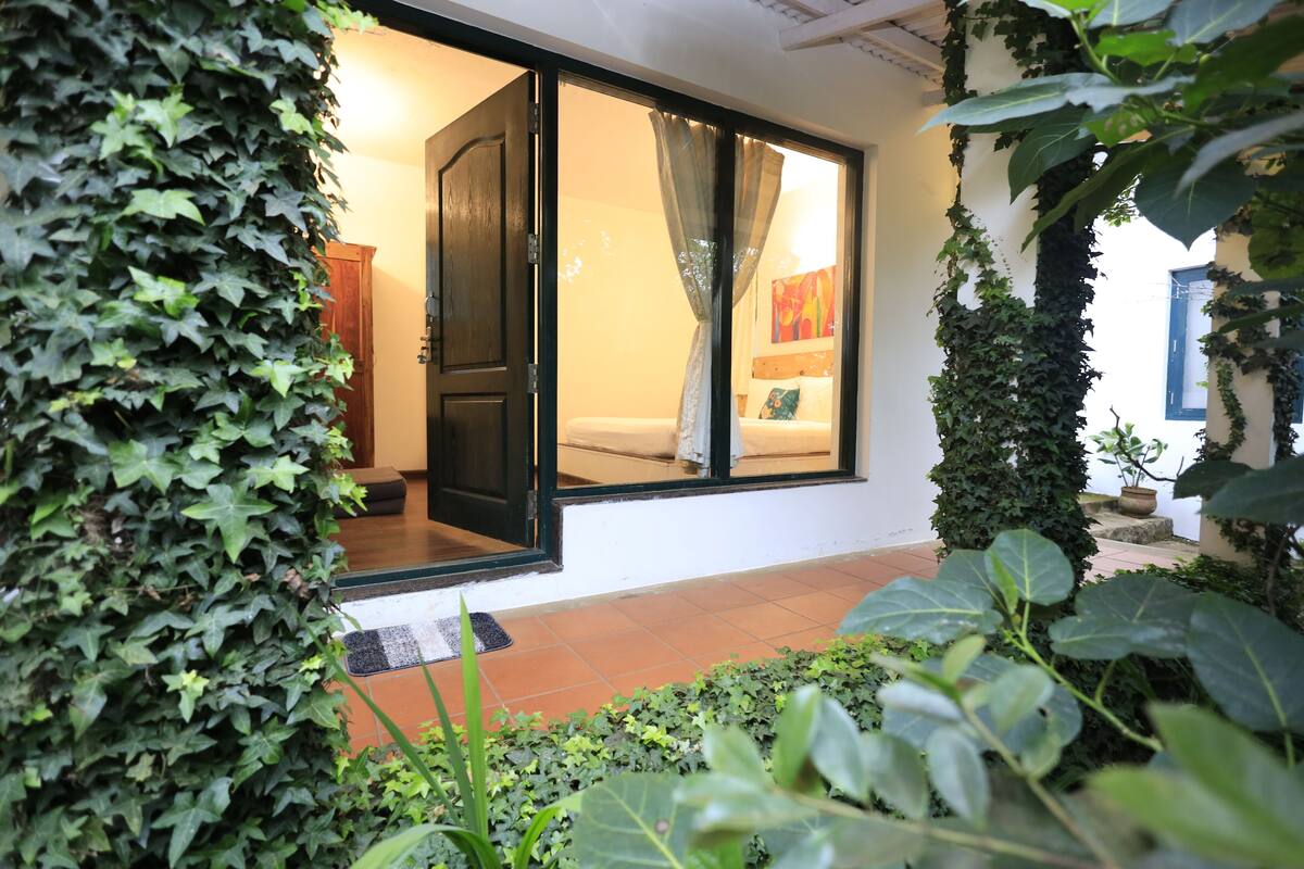 A room with a sliding glass door, a bed with a colorful blanket, and a small potted plant on the windowsill.