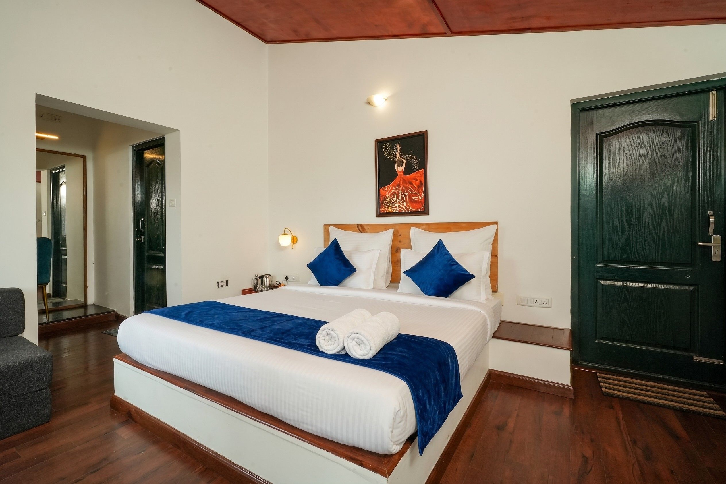 A hotel room with a bed, a nightstand, a wall-mounted lamp, a door, and a painting.