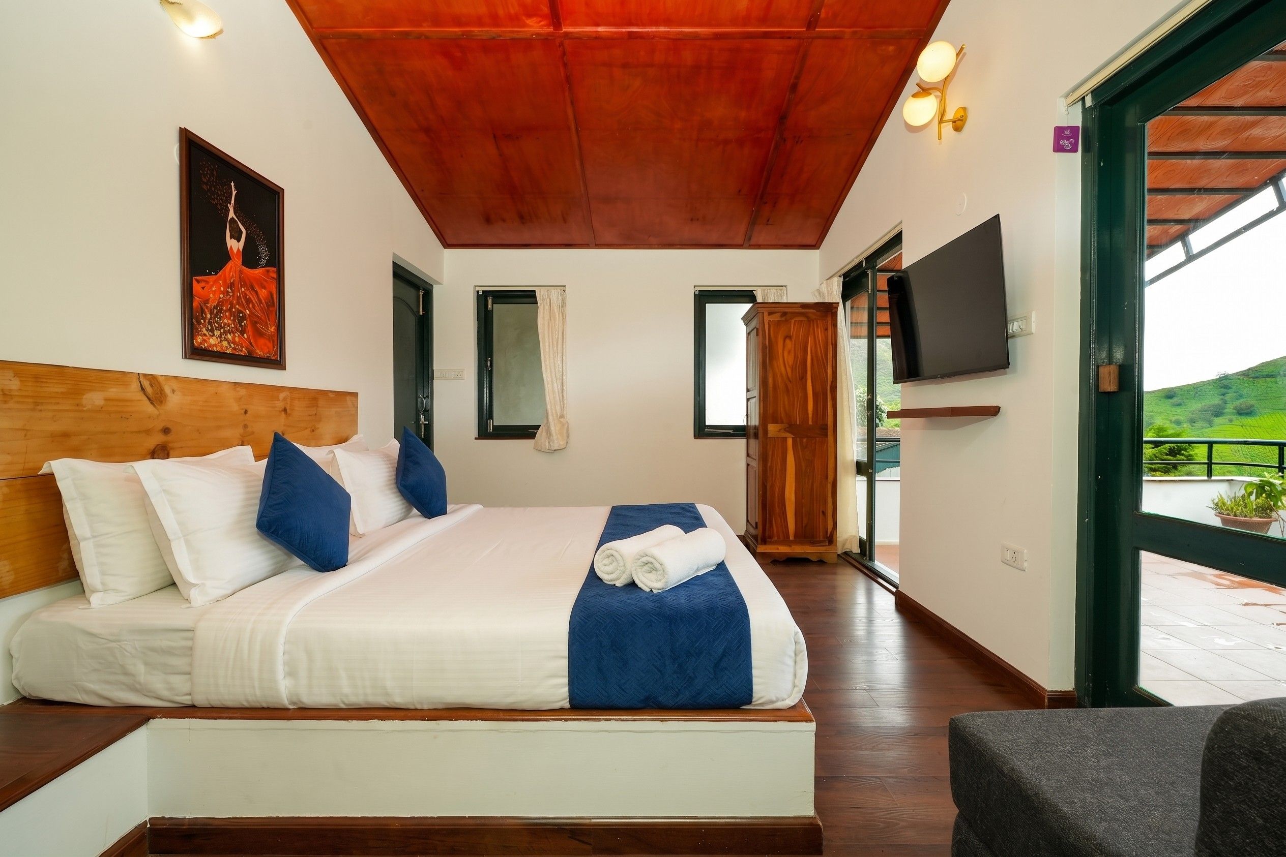 Une chambre à coucher avec une tête de lit en bois, un lit avec une literie blanche et bleue, un tableau accroché au mur et un téléviseur fixé au mur.