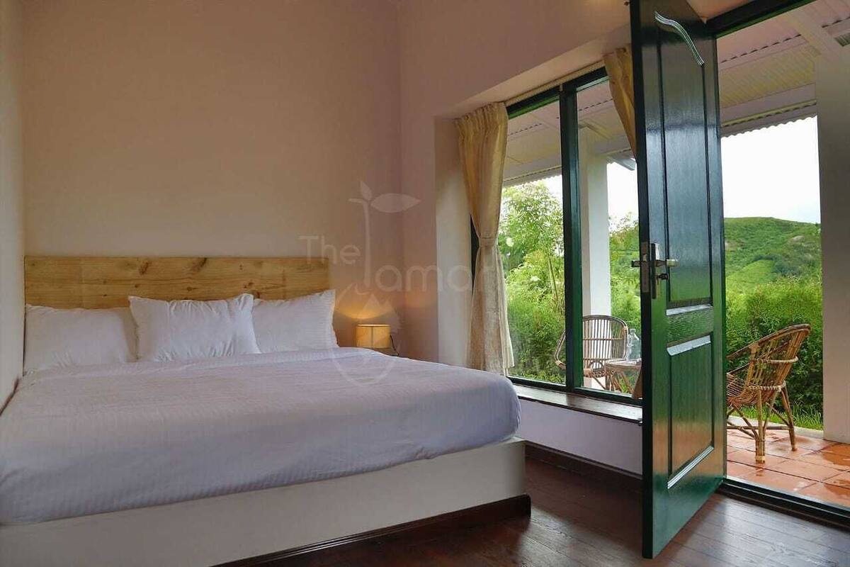 A bedroom with a large bed, a nightstand, and a window with a view of greenery.