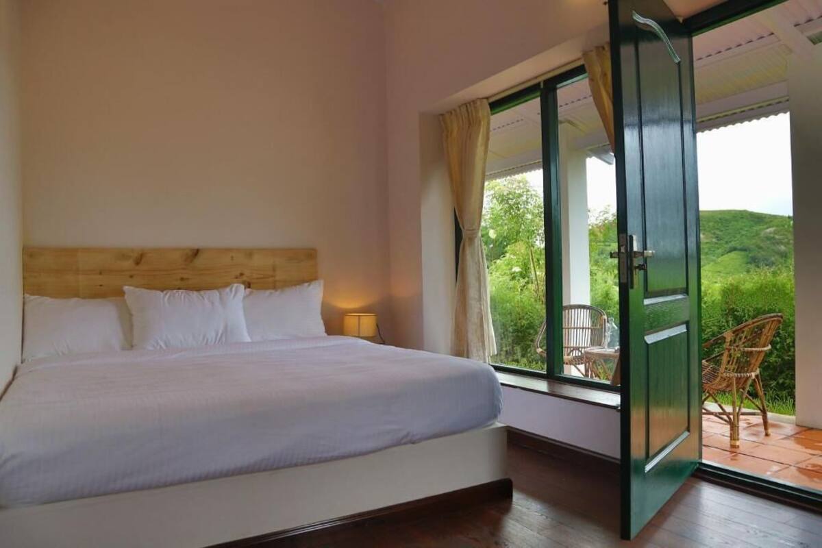 A bedroom with a bed, a window, and an open door leading to an outdoor area with chairs.