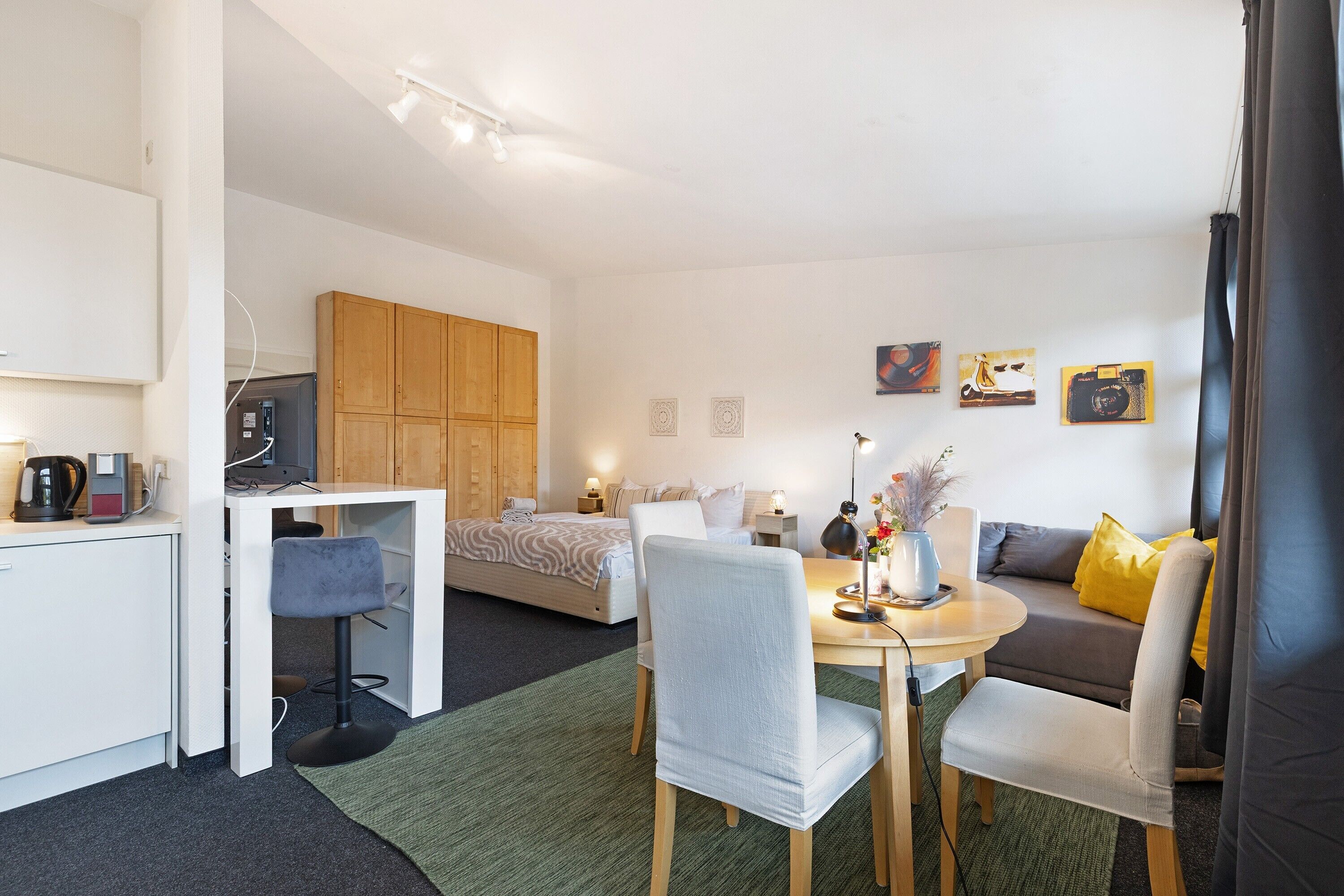 A modern, well-lit room with a bed, a desk, a dining table, and a sofa.