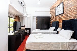 Habitación de hotel con dos camas, televisión, escritorio y pared de ladrillo.