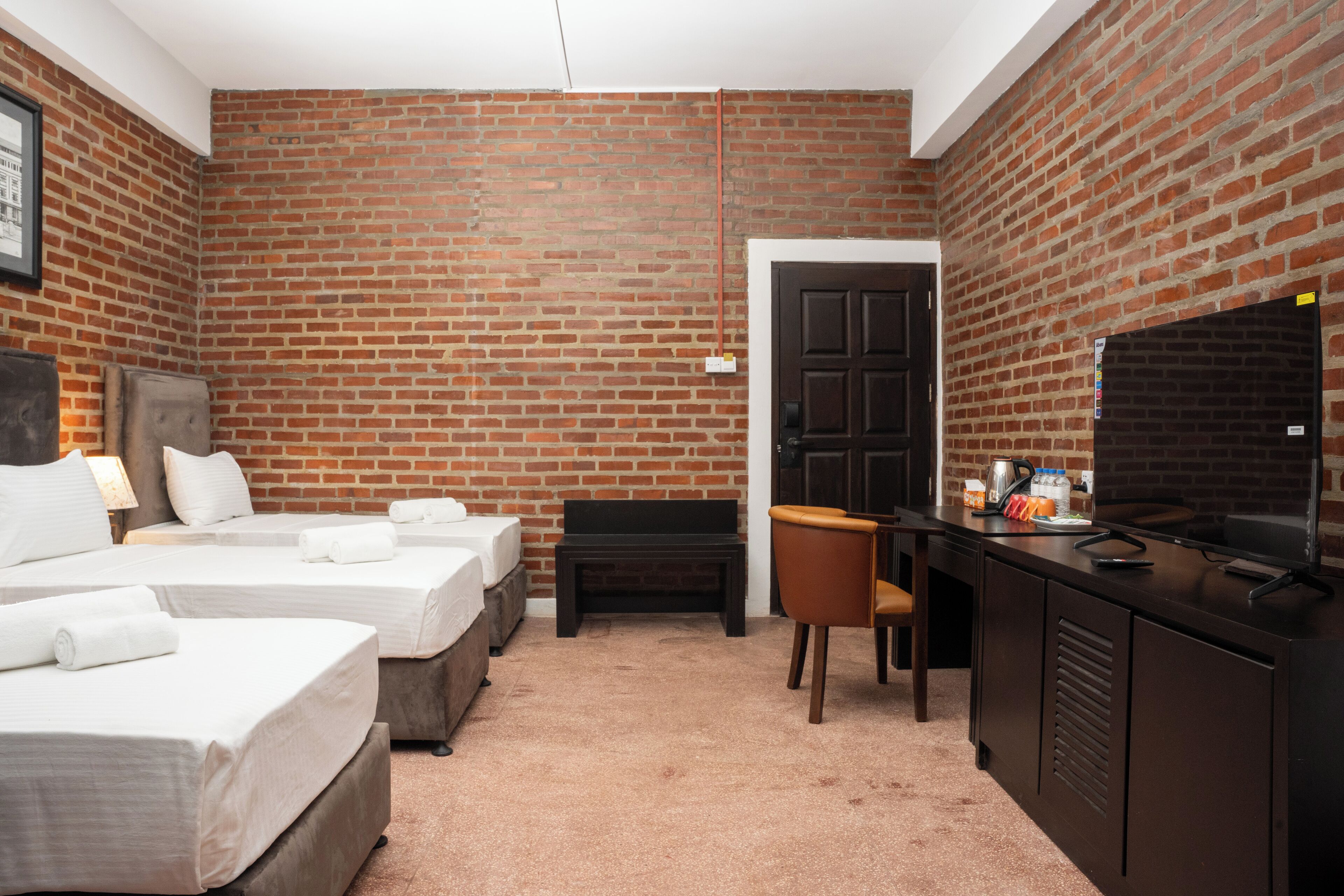 A hotel room with two beds, a desk, a television, and a brick wall.