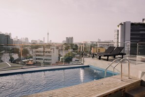 Una piscina en la azotea con vistas a la ciudad, sillas de descanso y barandilla de cristal.
