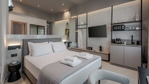A modern hotel room with a large bed, bedside tables, a flat-screen TV, a built-in kitchen area, and a seating area. - Amara Luxury Suites With Private Hot Tub (Chania)