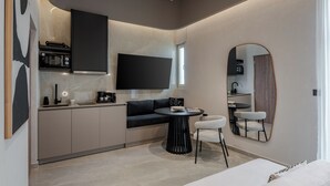 A modern kitchen with a built-in microwave, a black countertop, and a black sofa. There is a round table with two chairs and a large mirror on the wall. - Amara Luxury Suites With Private Hot Tub (Chania)