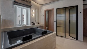 A modern bathroom with a large bathtub, a vanity with a mirror, and a shower area. - Amara Luxury Suites With Private Hot Tub (Chania)