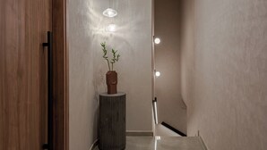 A modern hallway with a wooden door, a tall vase with plants, and pendant lights. - Amara Luxury Suites With Private Hot Tub (Chania)