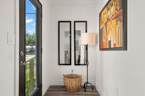 A hallway with a large window, a wicker basket, two framed mirrors, a floor lamp, and a painting on the wall.