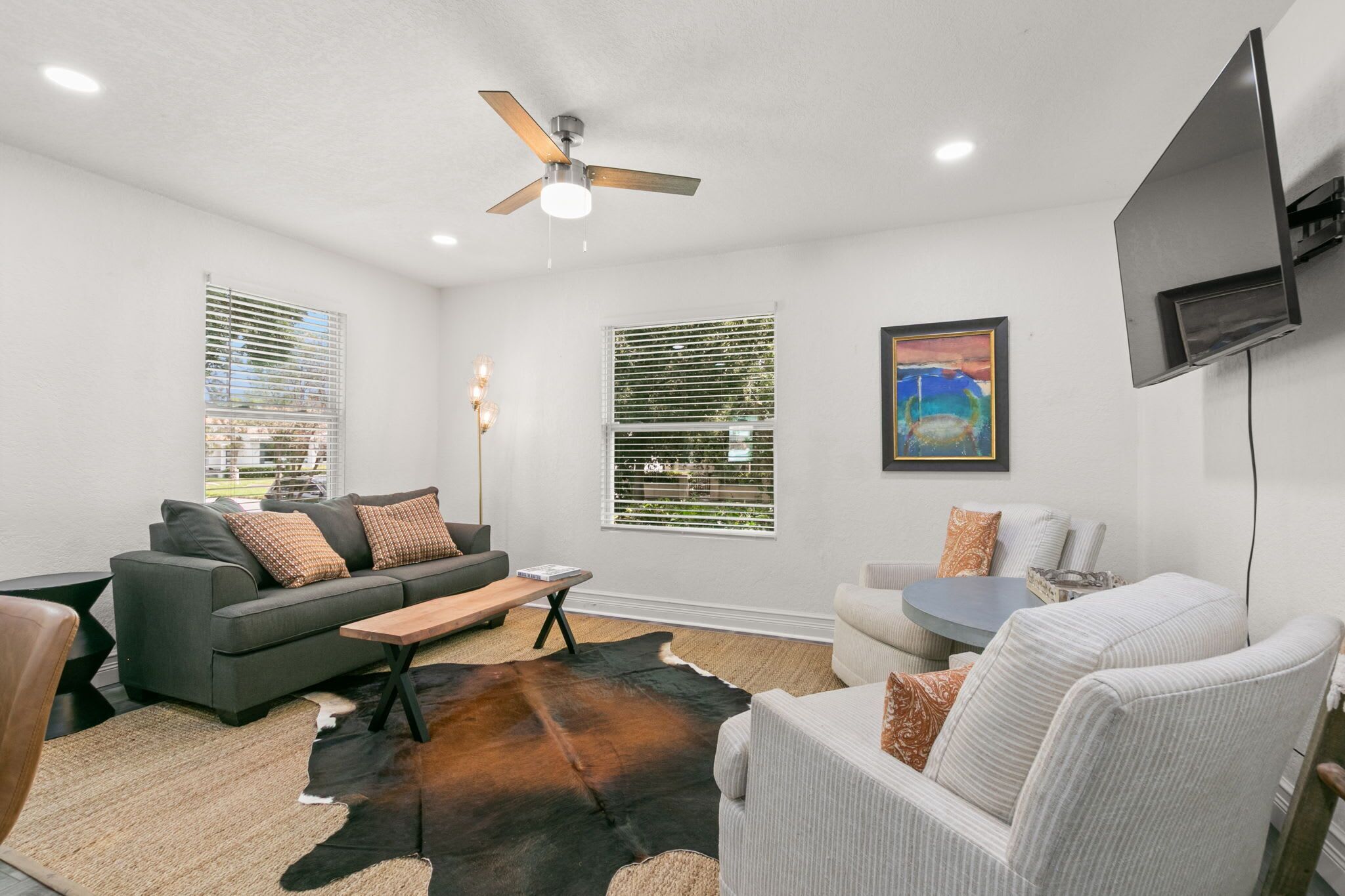 A living room with a gray sofa, a white armchair, a coffee table, and a TV mounted on the wall.