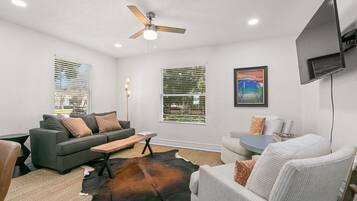 A living room with a gray sofa, a white armchair, a coffee table, and a TV mounted on the wall.
